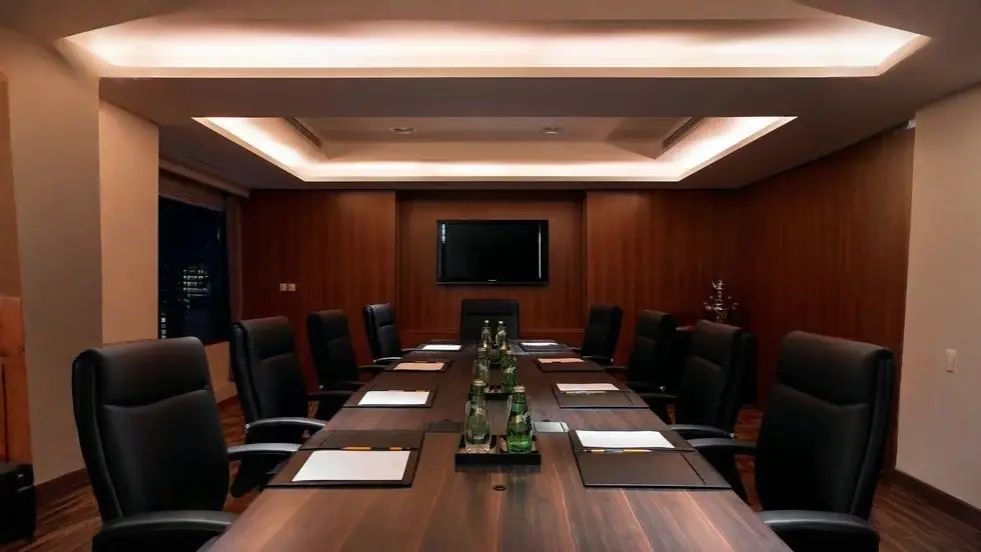 Core Principles of Backcasting A formal boardroom with a long wooden table, black leather chairs, warm recessed lighting, and a wall-mounted screen — representing high-level strategic planning where we discus core principle of backcasting.